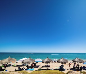 Ein Strand mit Reetdachschirmen, Liegestühlen und entspannten Menschen.
