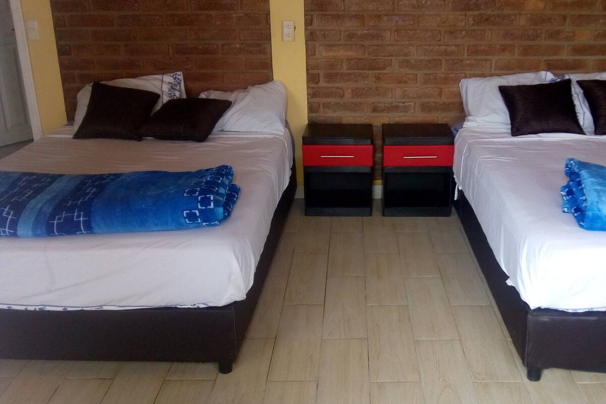 Une chambre d’hôtel avec deux lits, chacun doté d’une tête de lit sombre, de draps blancs et d’oreillers à motifs bleus. On trouve des tiroirs de rangement rouges et noirs sous les lits.