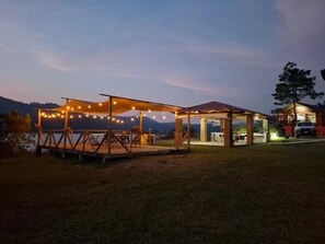 A covered outdoor area with string lights, a wooden deck, and a building with a red roof. - Cabañas Junkolal (La Trinitaria)