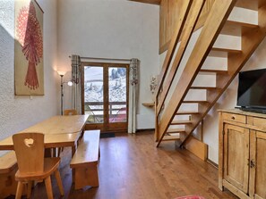 A wooden interior with a dining table, benches, a TV on a wooden cabinet, and a staircase.