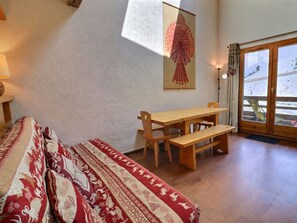 A room with a bed, a wooden table with benches, a wall-mounted lamp, and a door leading to a balcony.