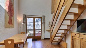 A wooden interior with a dining table, benches, a TV on a wooden cabinet, and a staircase. - Family duplex on the slopes, ideal for 7 people (Méribel)