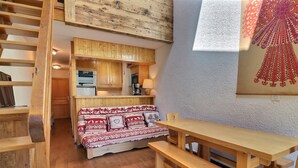 A cozy room with a wooden bench, a sofa with patterned cushions, a wooden table, and a kitchen area with wooden cabinets. - Family duplex on the slopes, ideal for 7 people (Méribel)