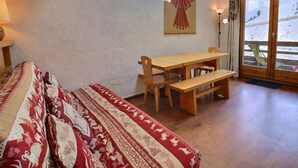 A room with a bed, a wooden table with benches, a wall-mounted lamp, and a door leading to a balcony. - Family duplex on the slopes, ideal for 7 people (Méribel)