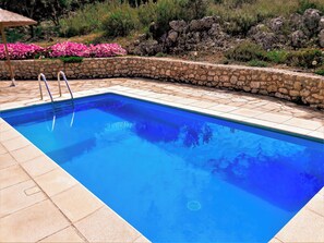 Ein rechteckiger Pool mit klarem, blauem Wasser, umgeben von einer Steinmauer und einer gefliesten Terrasse.
