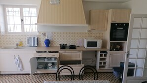 Une cuisine compacte équipée d’un four à micro-ondes, d’une cuisinière et d’un évier. On y trouve une table à manger avec des chaises, et le sol est recouvert de carreaux disposés selon un motif géométrique.