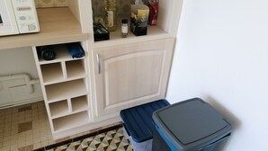 Une cuisine compacte équipée d’un four à micro-ondes, d’étagères et d’une poubelle.