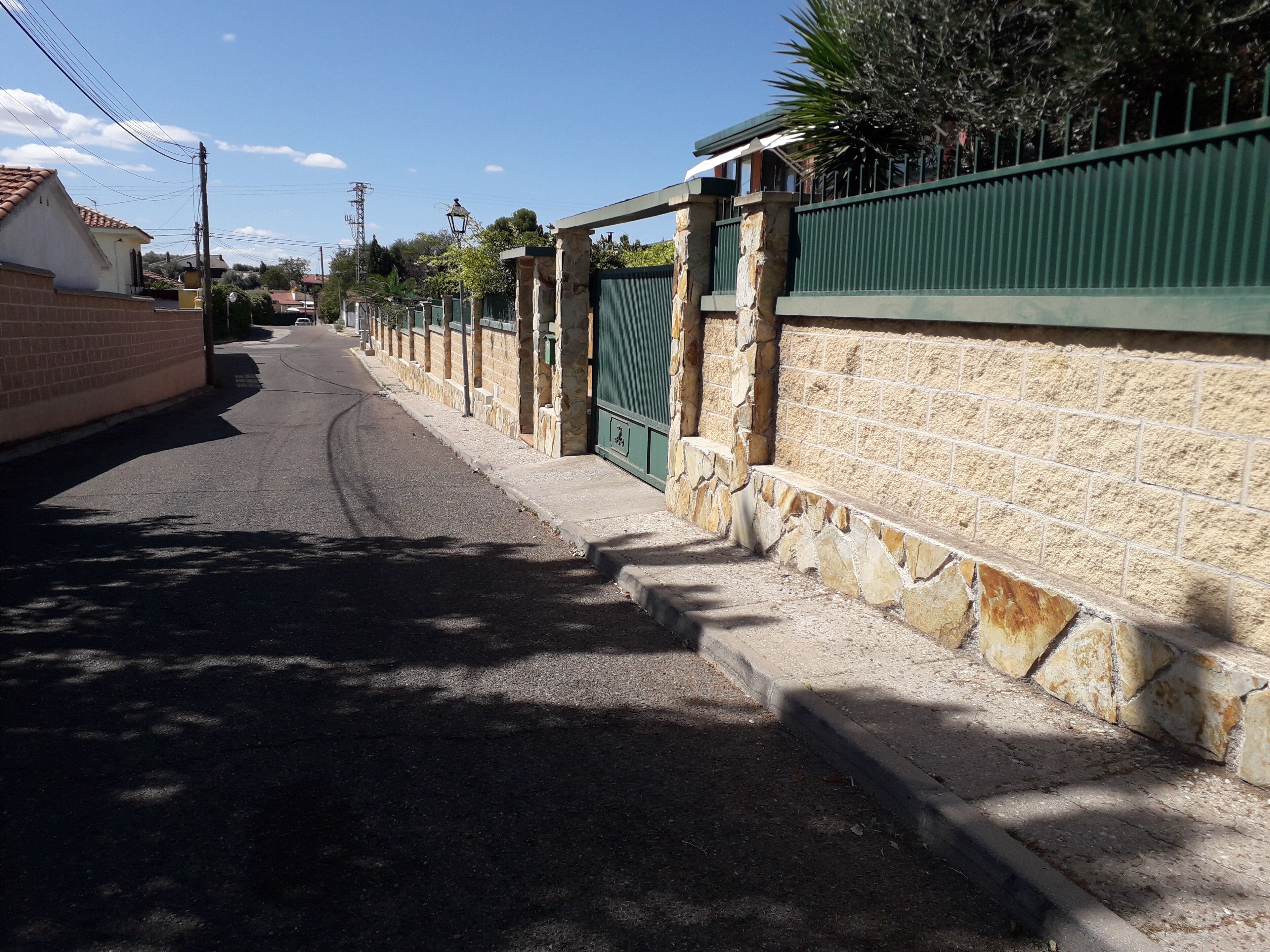 A narrow street with stone walls and a green fence on one side.