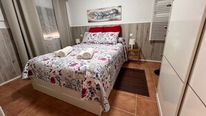 A neatly made bed with floral bedding, a red headboard, and a bedside lamp.
