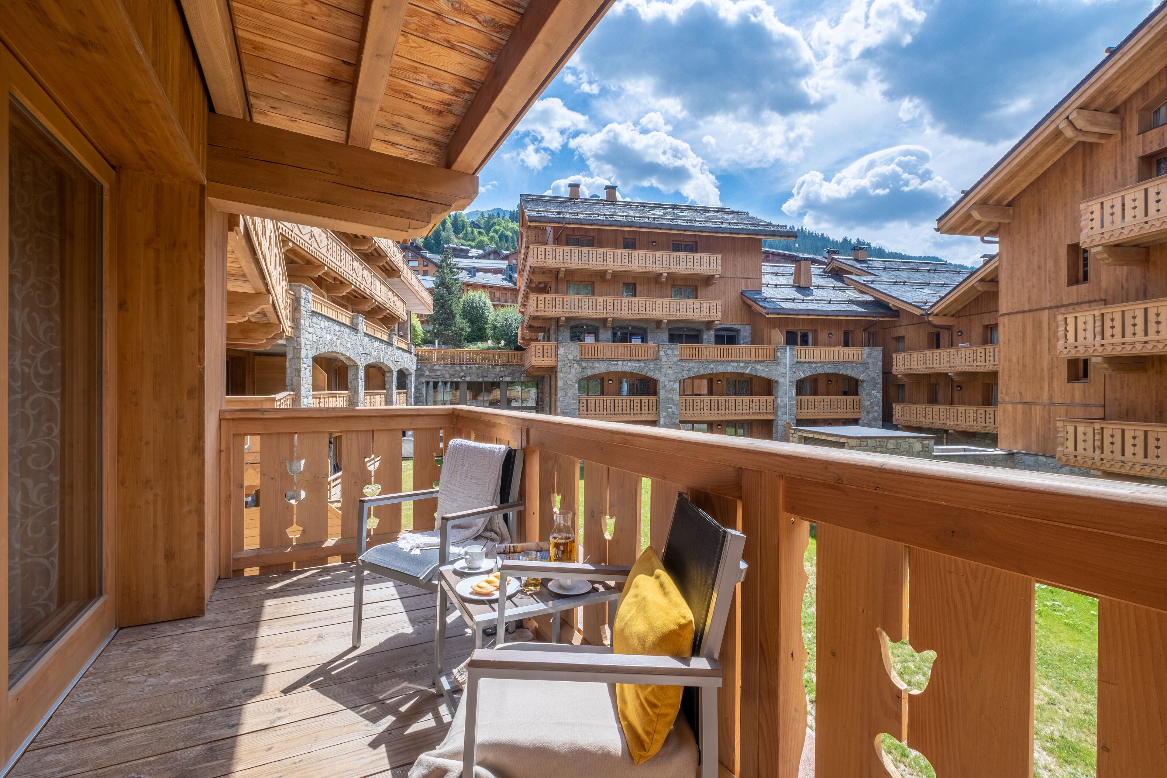 Un balcon en bois, agrémenté d’une table et de chaises, qui offre une vue sur un village aux bâtiments traditionnels.