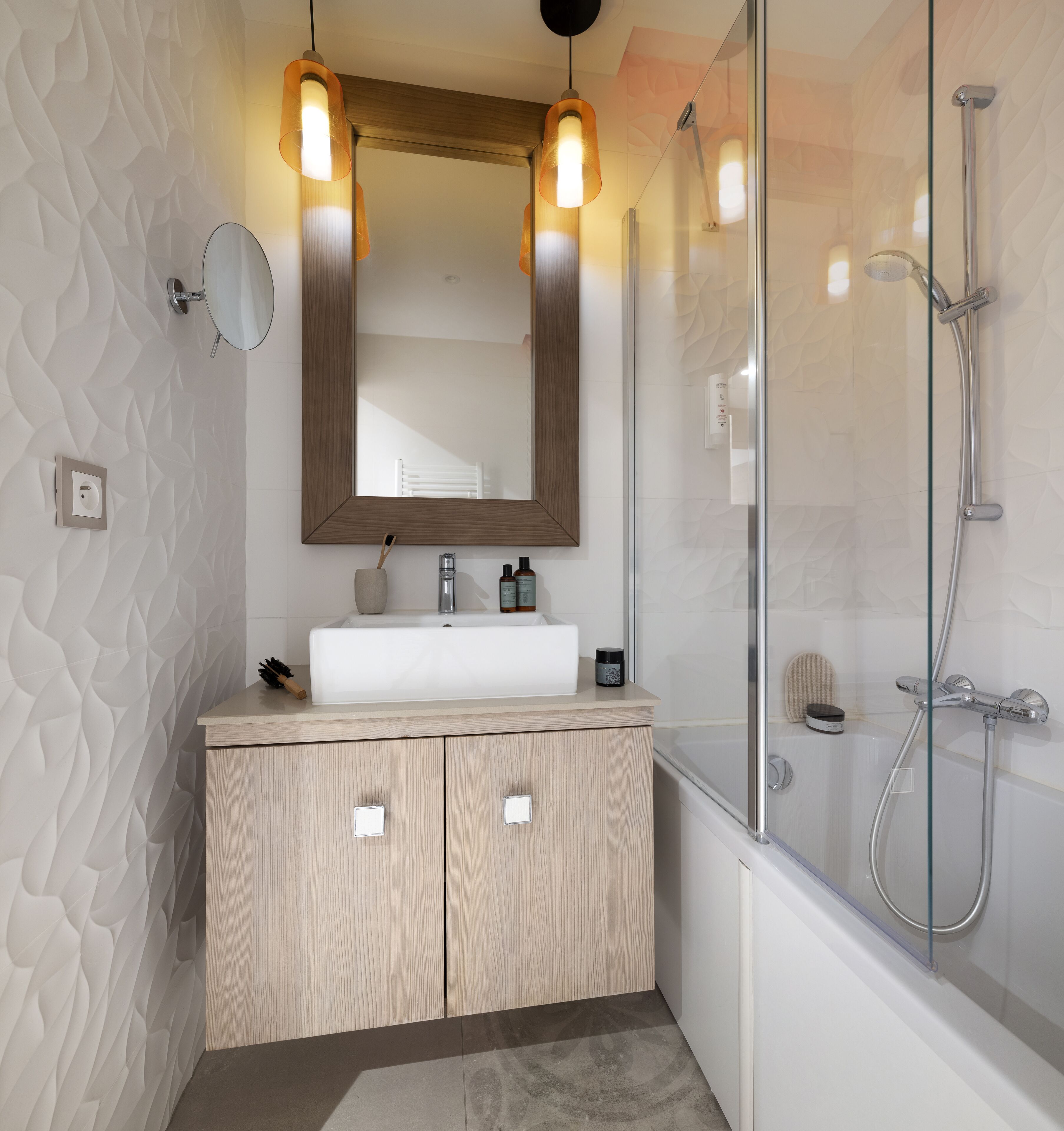 Ein modernes Badezimmer mit einem Holzwaschtisch, einem großen Spiegel, Pendelleuchten, einer Glasdusche und einer Badewanne.