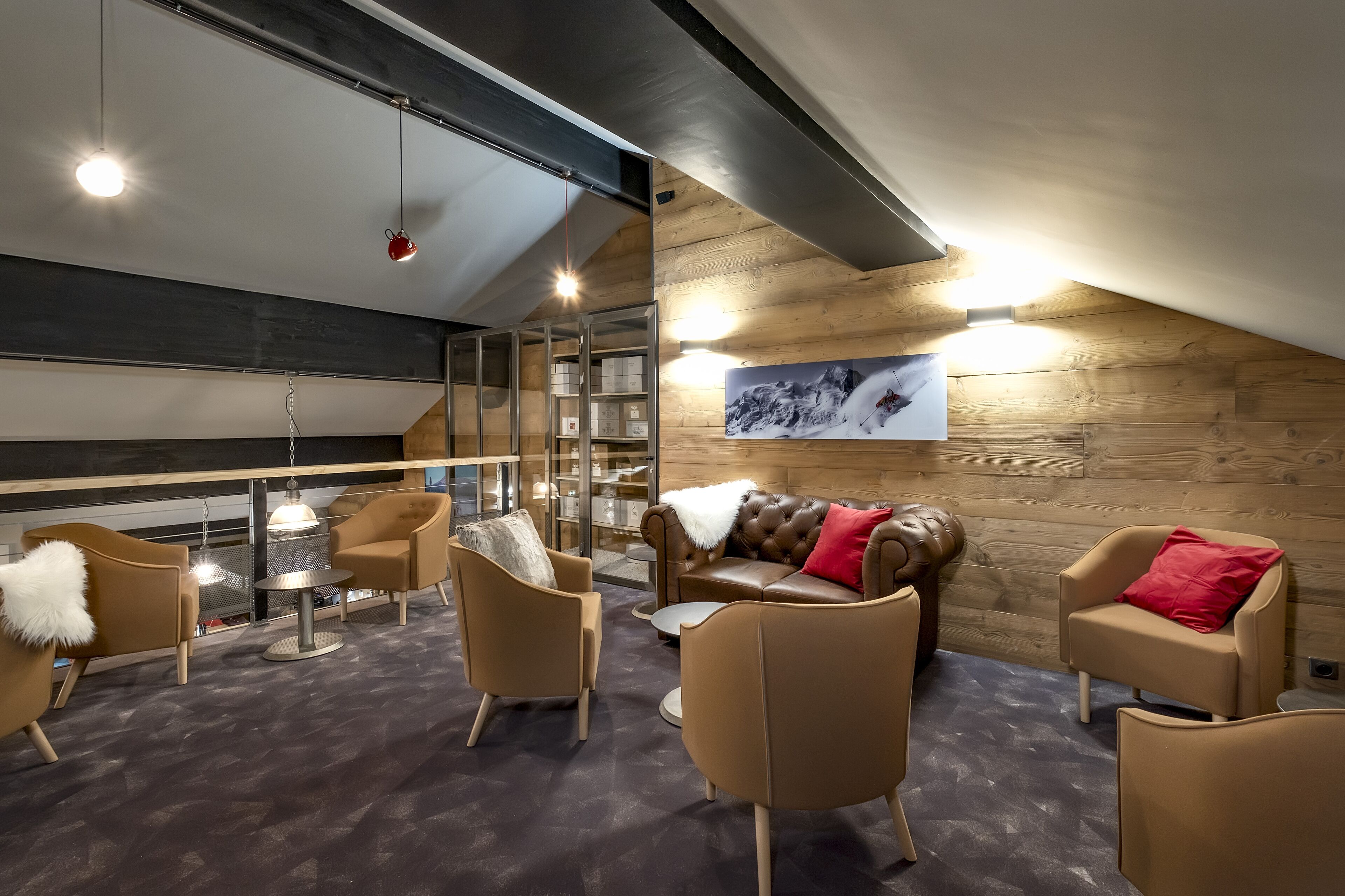A modern interior with a loft-style ceiling, leather sofas with red and white cushions, and a large framed picture on the wall.