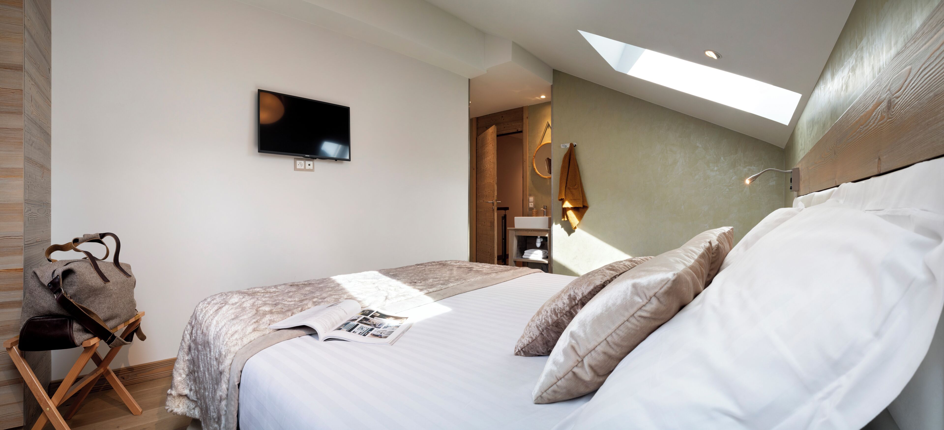 A bedroom with a bed, a flat-screen TV, a skylight, and a wooden headboard.