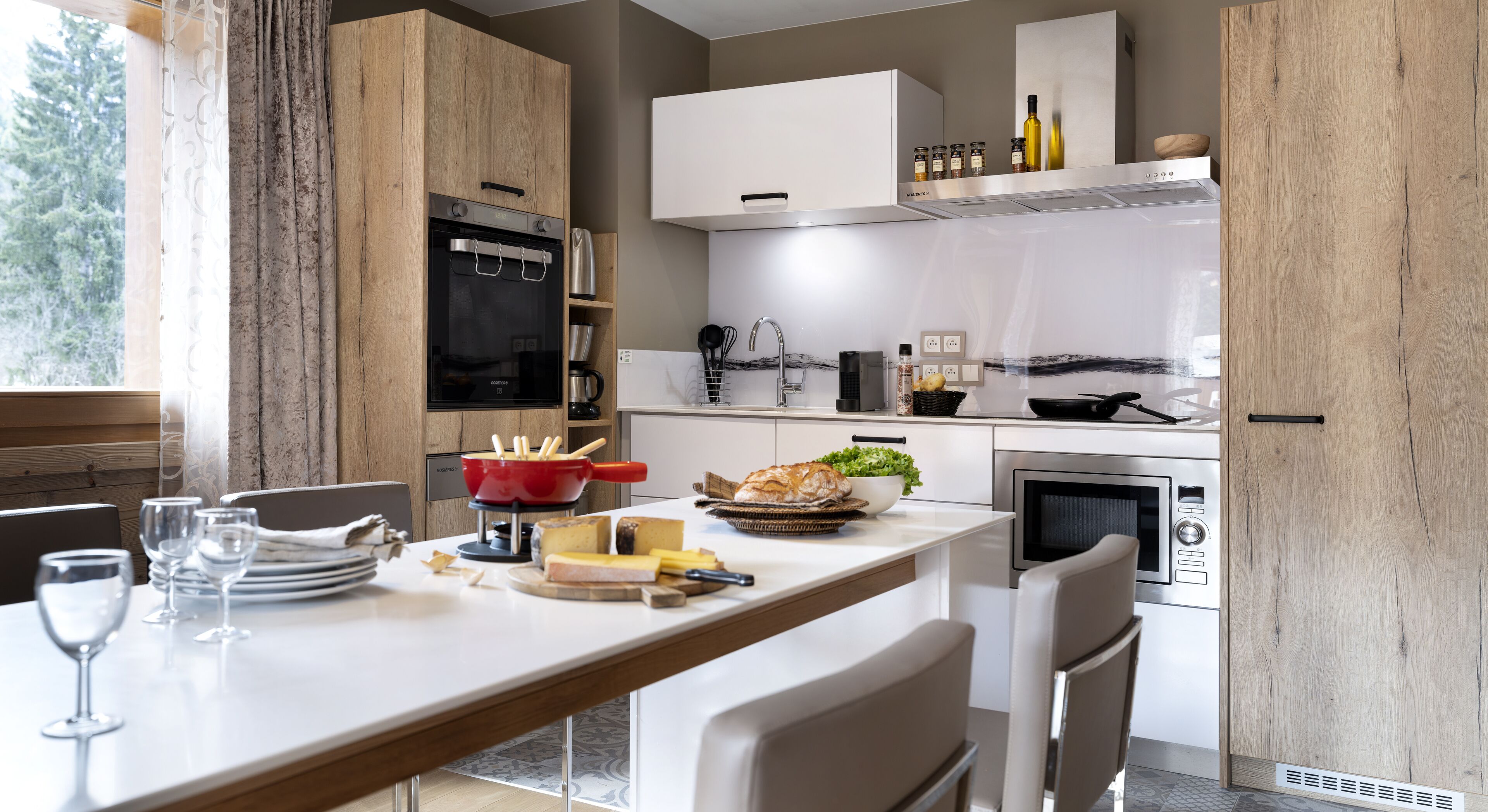 A modern kitchen with wooden cabinets, a built-in oven, a microwave, and a dining area with a table set for two.