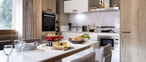 A modern kitchen with wooden cabinets, a built-in oven, a microwave, and a dining area with a table set for two.