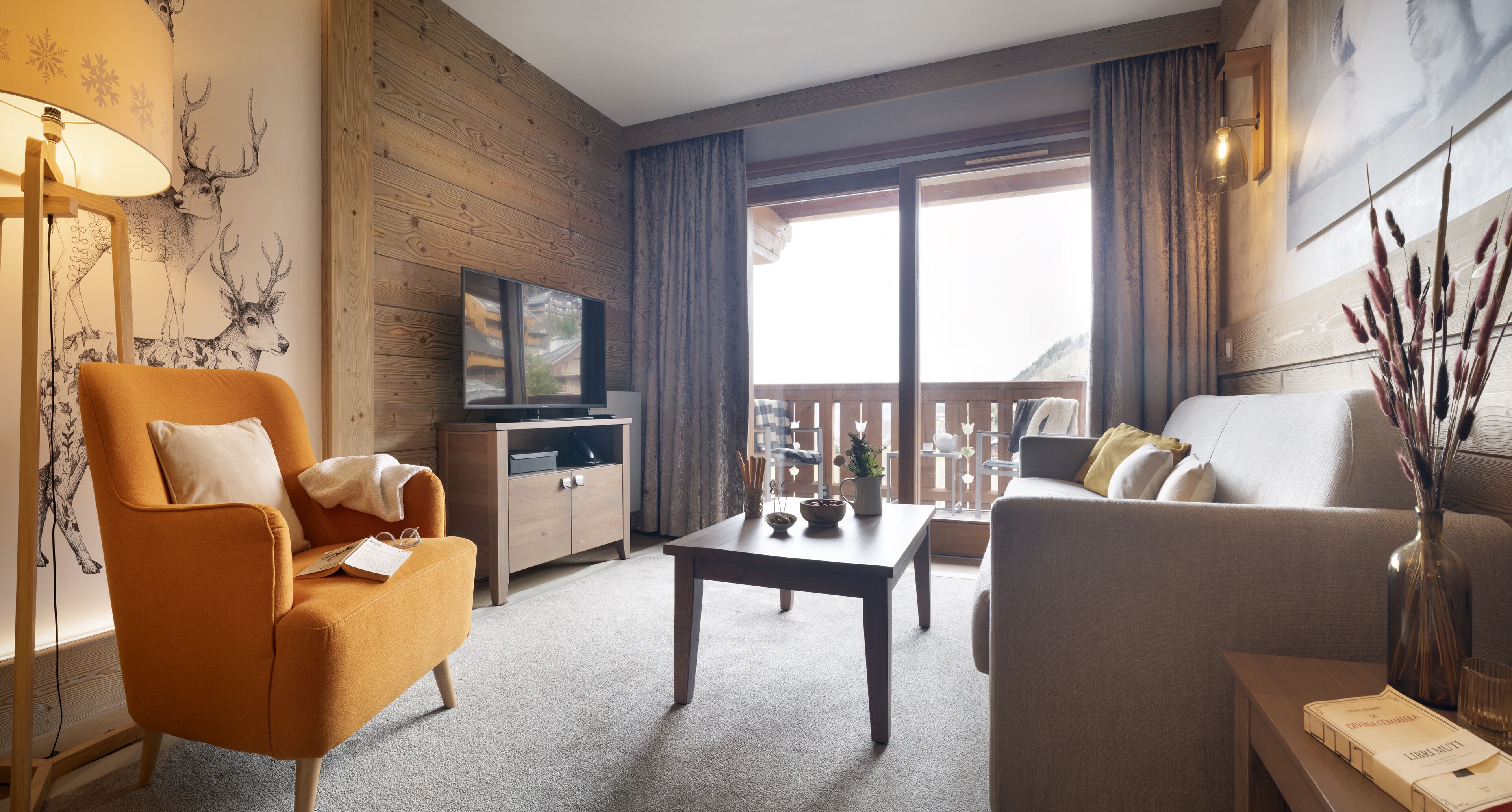 Una sala de estar acogedora con un sofá, un sillón y una mesita de centro. Un televisor está montado en la pared, y hay una ventana con vistas al exterior.
