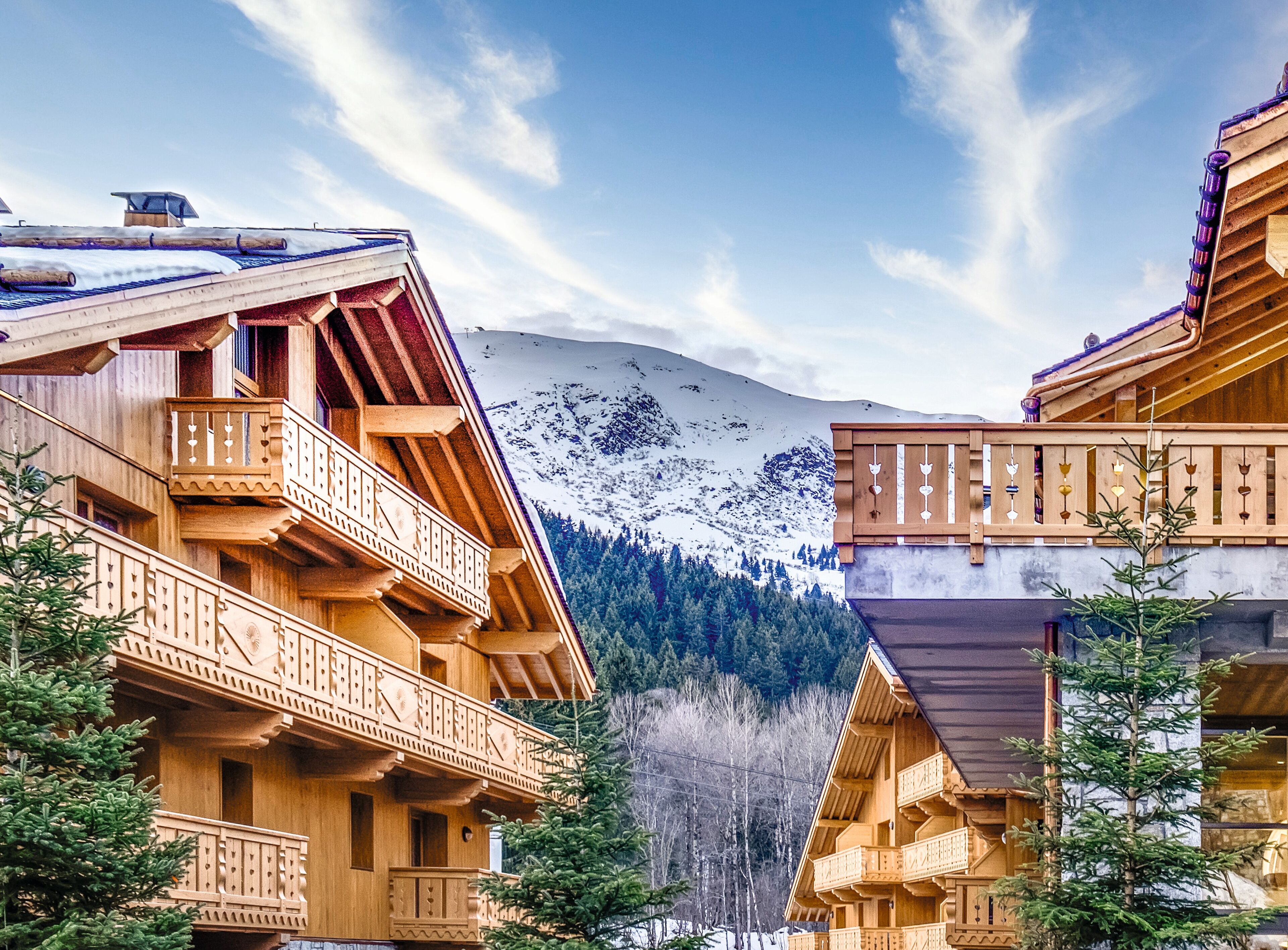 A wooden chalet with balconies, a snowy mountain backdrop, and a forested valley.