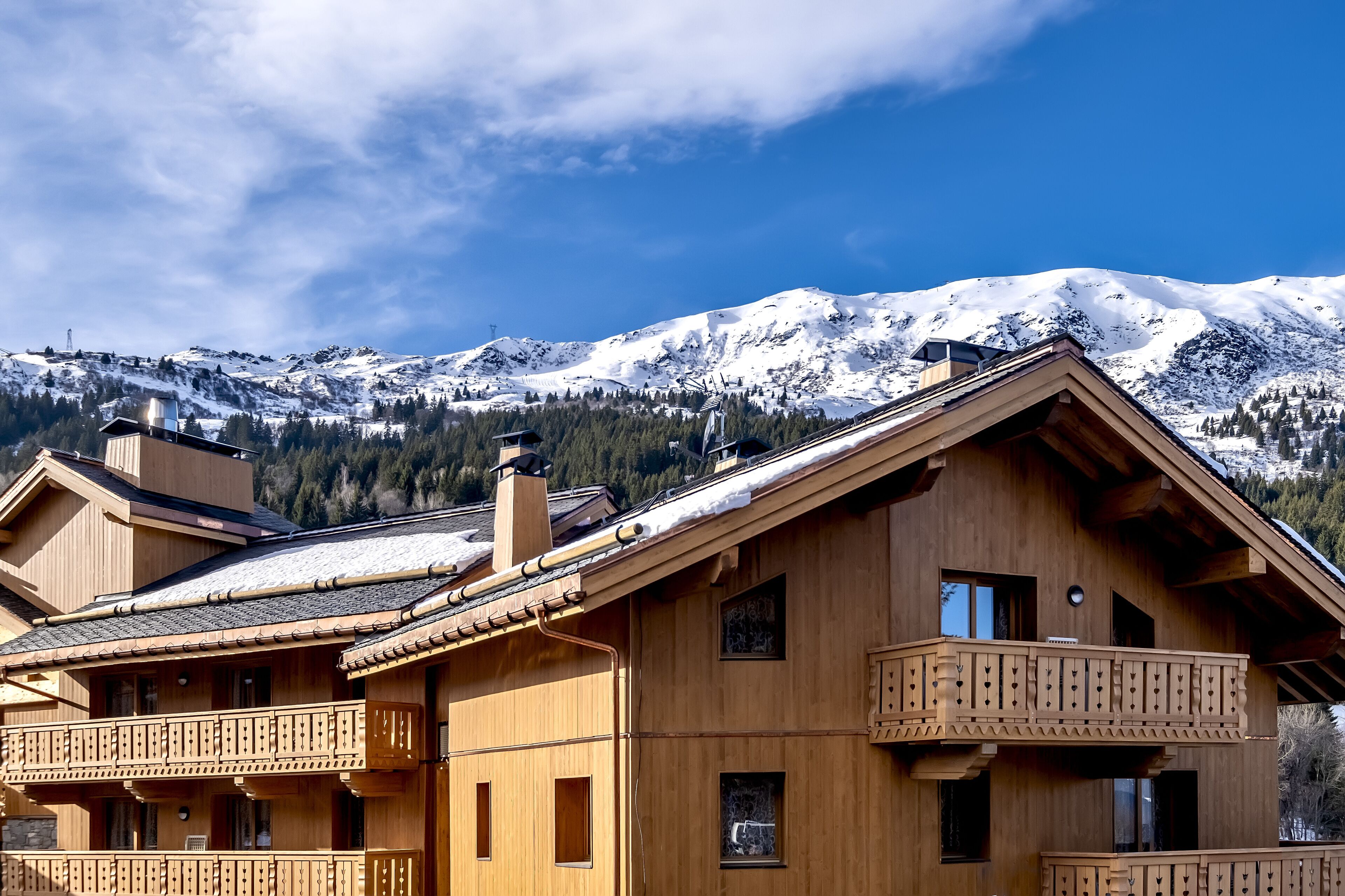 Una cabaña de madera con balcones, con montañas nevadas y un cielo despejado de fondo.