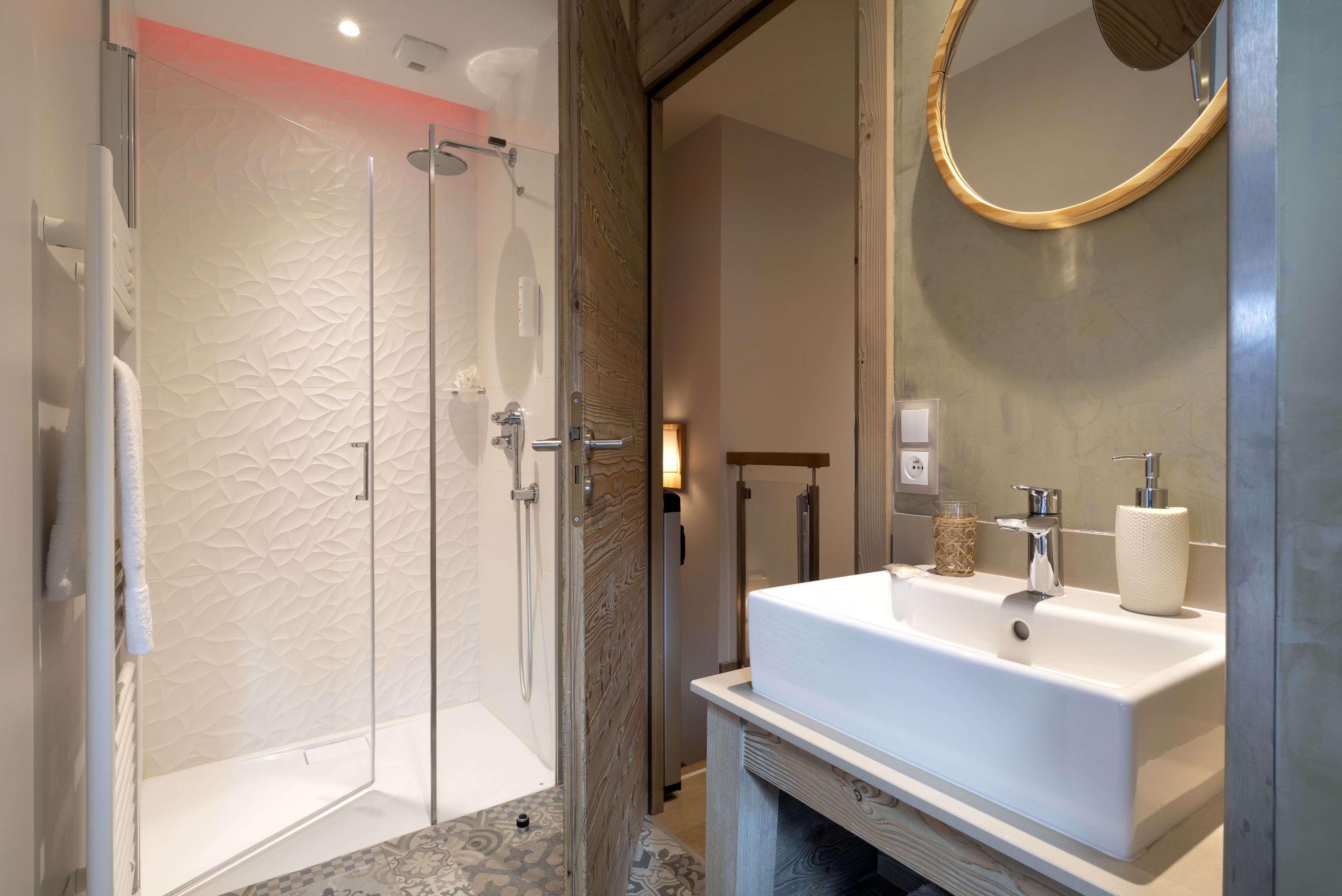 A modern bathroom with a glass-enclosed shower, a white sink with a mirror, and a wooden vanity.