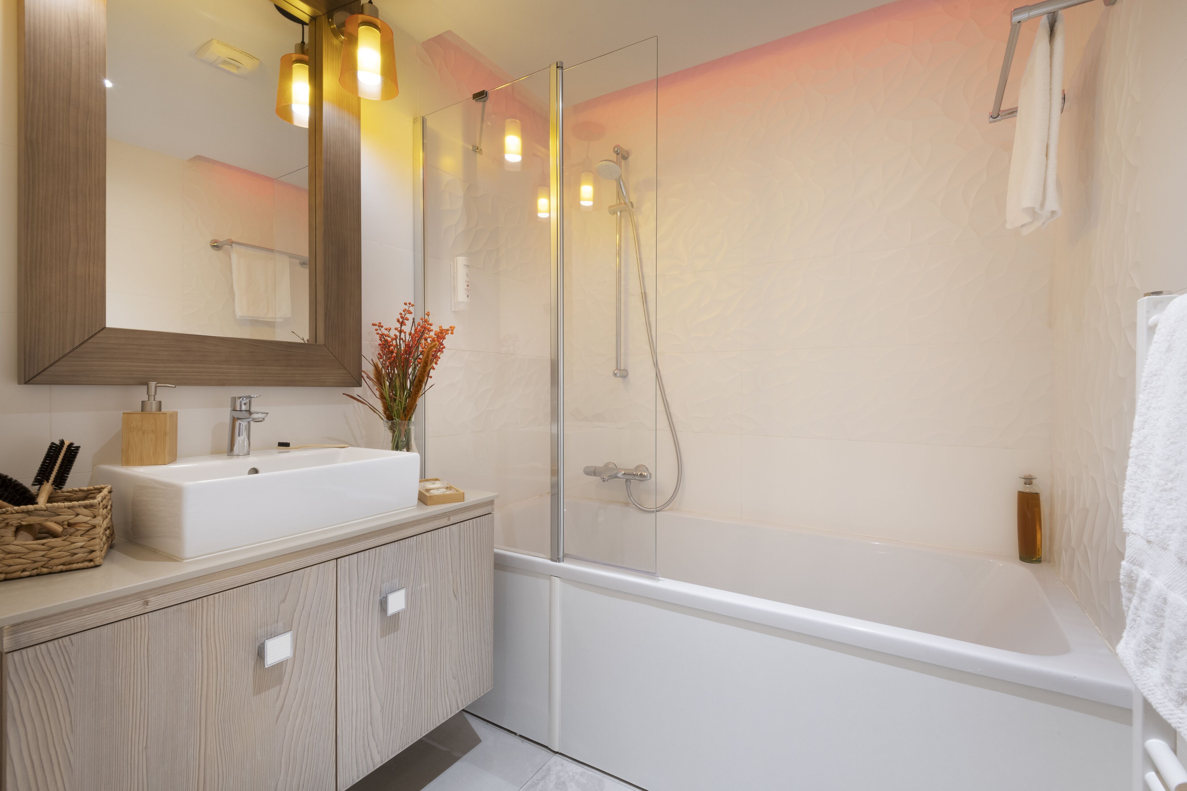 Un baño moderno con ducha acristalada, un lavamanos blanco y un espejo encima.