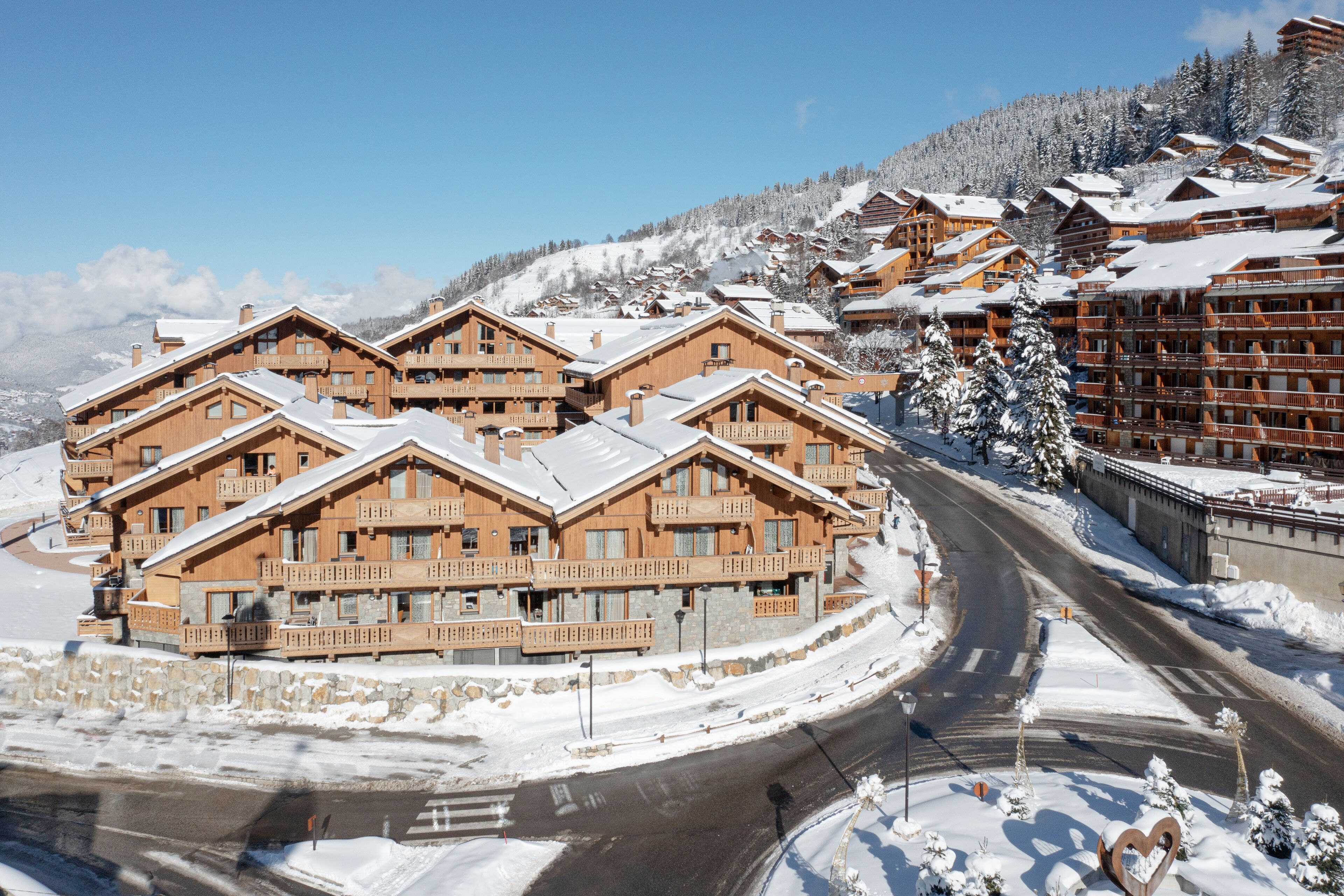 En grupp av träbyggnader i chaletstil med balkonger, omgivna av snötäckta sluttningar och en slingrande väg.
