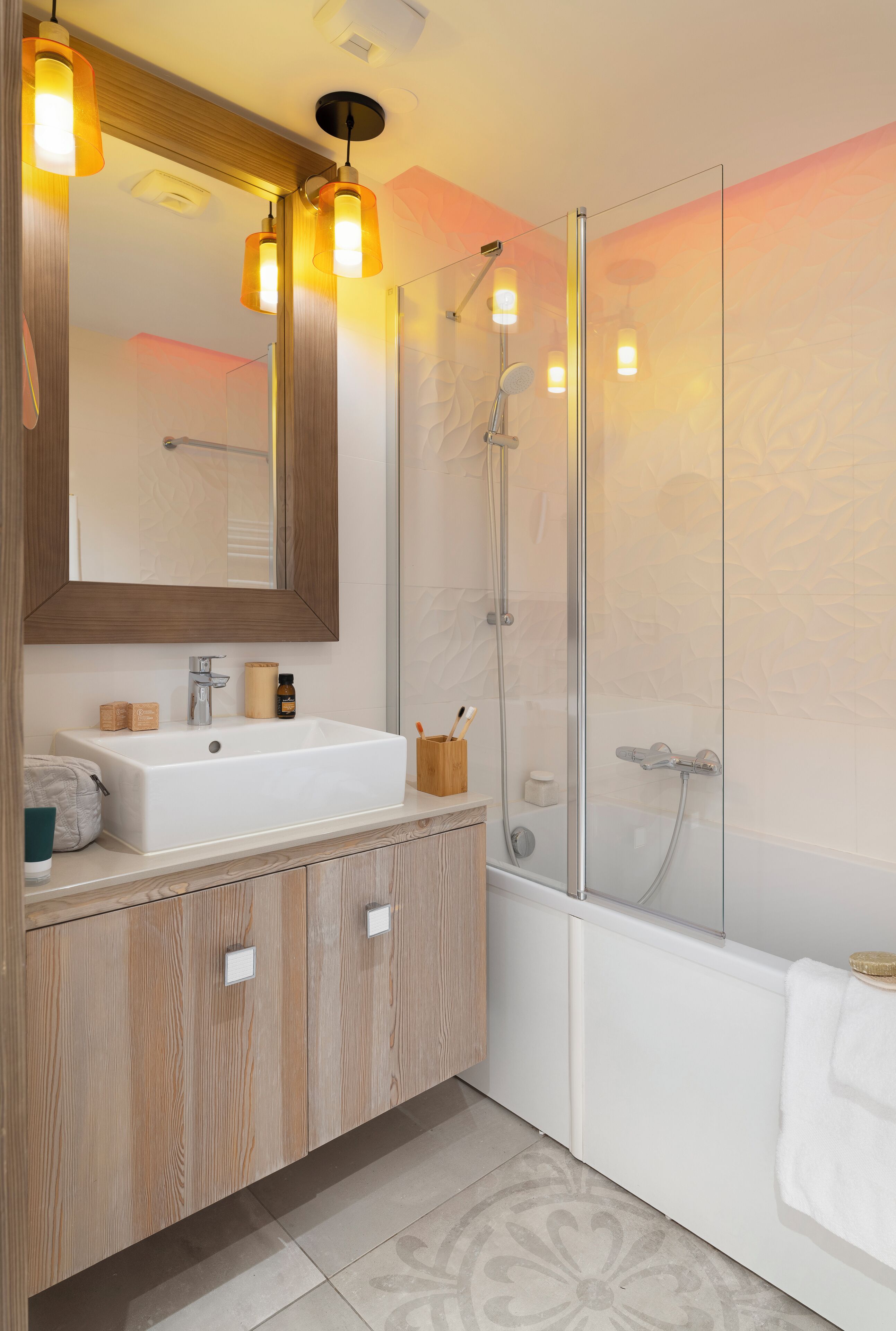 Un baño moderno con un espejo grande, armarios de madera, un lavabo blanco y una cabina de ducha de vidrio.