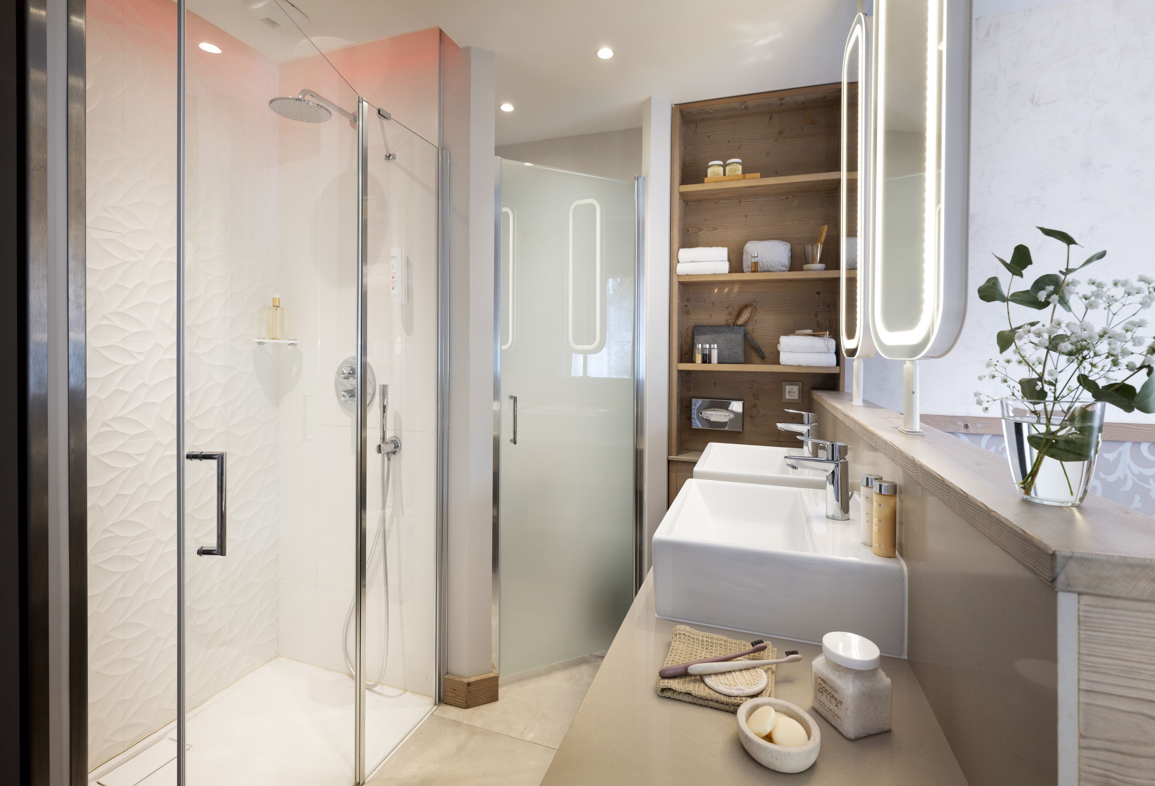 Et moderne badeværelse med et glasvægshus, et toiletbord med et stort spejl og en hylde med toiletartikler.