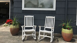 Twee schommelstoelen voor een huis met een raam erboven.