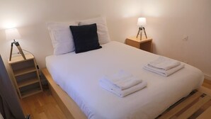 A neatly made bed with white linens and folded towels, two bedside lamps, and a wooden nightstand. - Sunny Dussoubs I Unique 1-BR loft in Montorgueil (Paris)