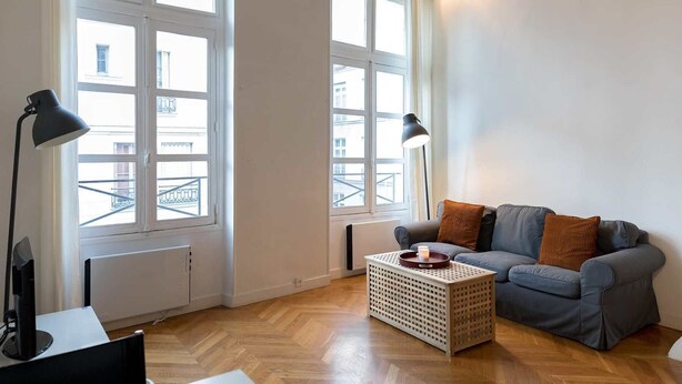 A modern living room with a grey sofa, two black floor lamps, a wooden coffee table, and large windows with white frames. - Sunny Dussoubs I Unique 1-BR loft in Montorgueil (Paris)