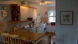 Una cucina con un tavolo e sedie in legno, una lavatrice, un fornello e un forno a microonde.