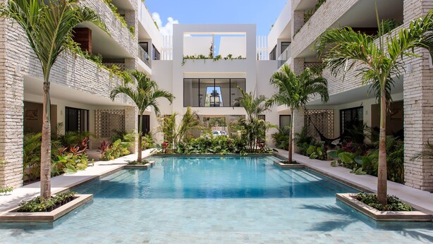 A modern building with a central pool surrounded by lush greenery and palm trees. - Beautifully Minimalistic Studio Wrapped in Nature by Stella Rentals (Tulum)