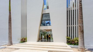 A modern building with a central glass entrance, flanked by tall palm trees and a clear sky. - Beautifully Minimalistic Studio Wrapped in Nature by Stella Rentals (Tulum)