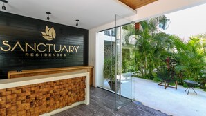 A reception area with a wooden reception desk, a black wall with 'SANCTUARY RESIDENCES' signage, and a glass door leading to a tropical garden. - Beautifully Minimalistic Studio Wrapped in Nature by Stella Rentals (Tulum)