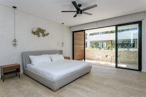 A modern bedroom with a large bed, a ceiling fan, and a sliding glass door leading to an outdoor patio. - Beautifully Minimalistic Studio Wrapped in Nature by Stella Rentals (Tulum)