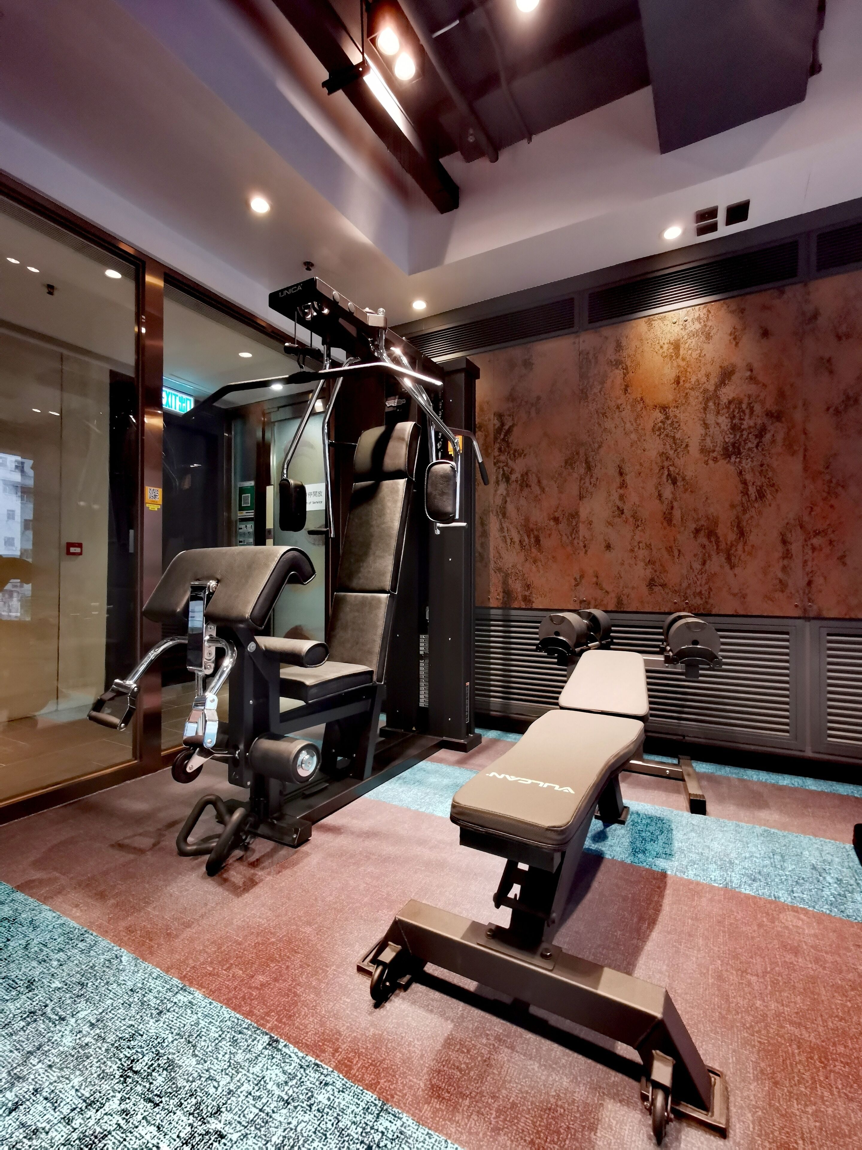 Uma academia com equipamentos de exercícios, um banco e uma parede com padrão texturizado.