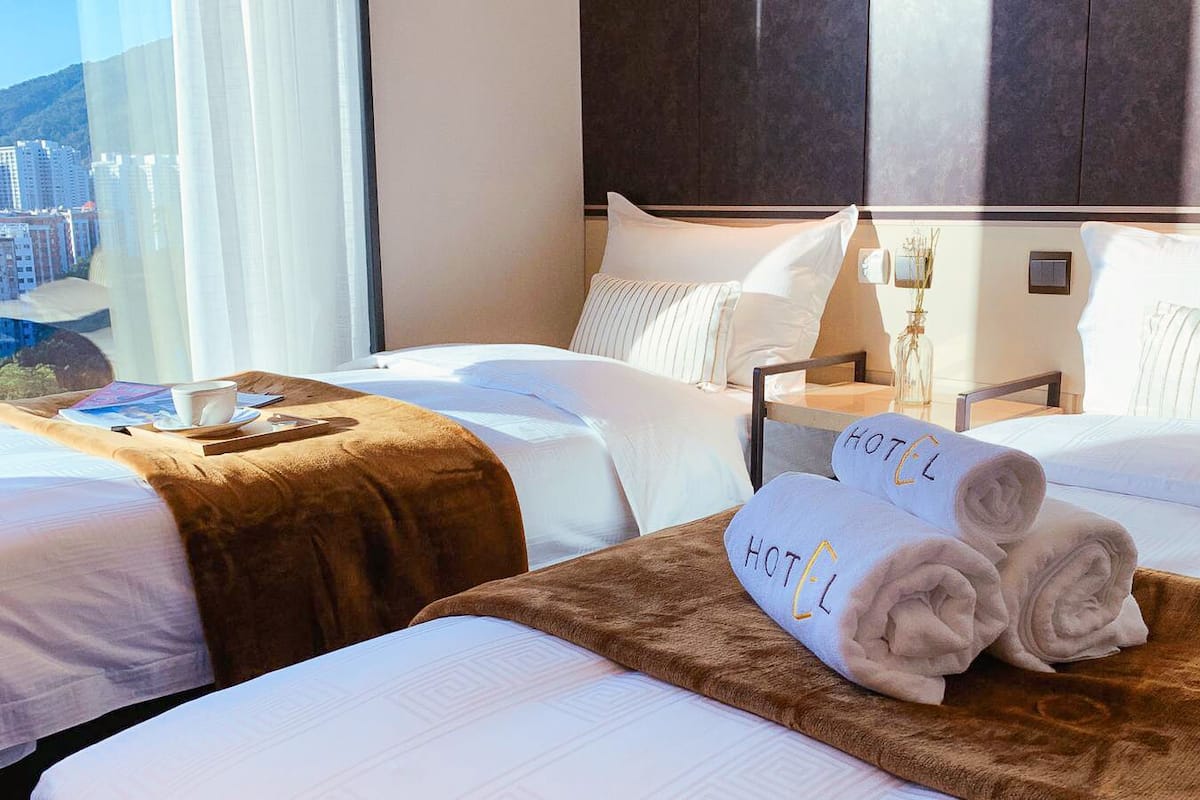 A hotel room with two beds, a wooden headboard, and a view of the cityscape.
