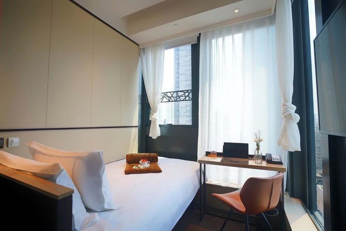 A modern hotel room with a bed, a desk, and a chair.