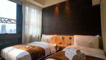 A hotel room with two beds, a city view, a window with curtains, and a nightstand with a vase of flowers.