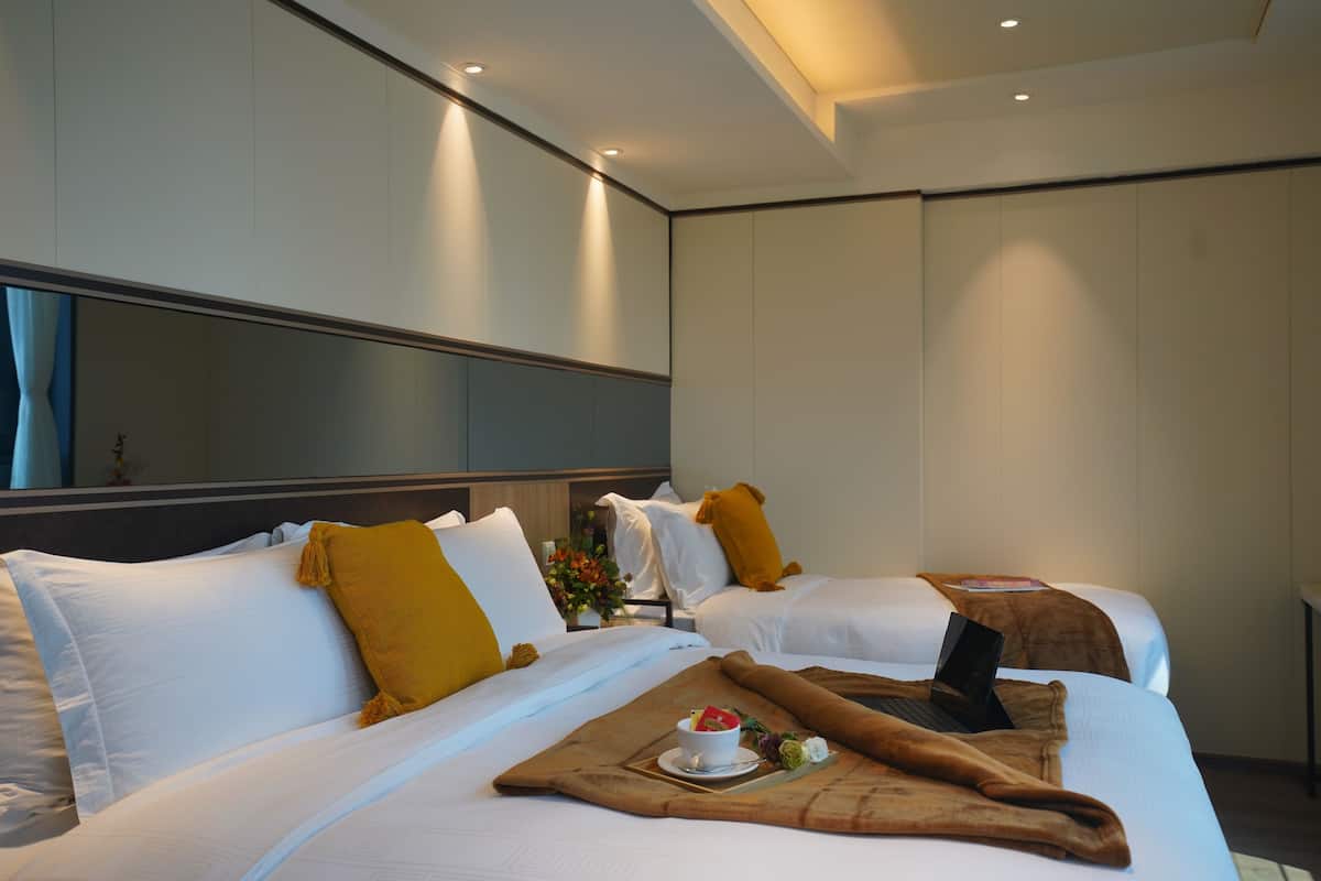 A hotel room with two beds, a laptop on one bed, and a breakfast tray on the other.