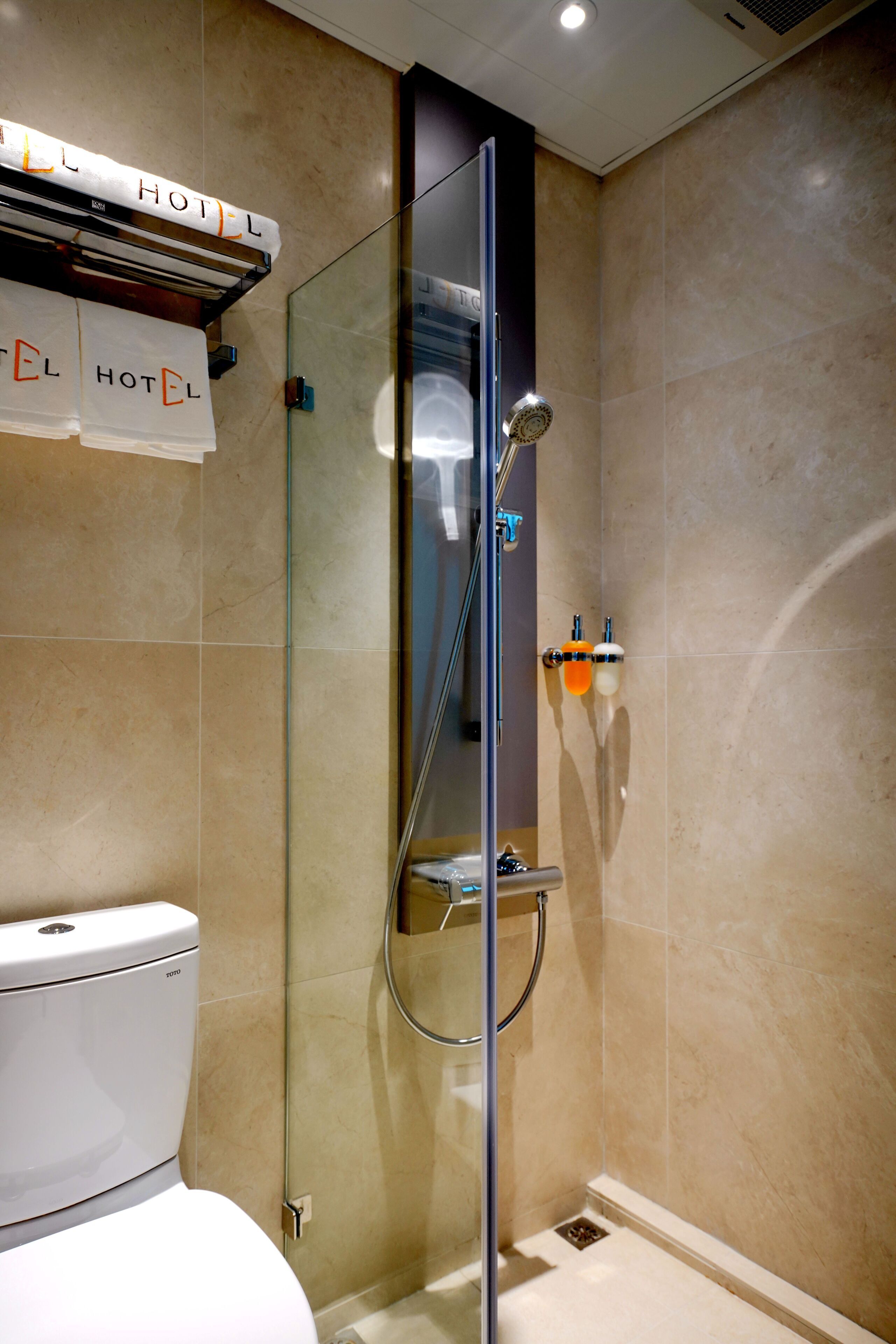 A modern bathroom with a glass-enclosed shower, a toilet, and a towel rack labeled "HOTEL".