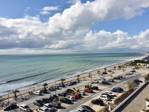 A coastal parking area with vehicles, a beach, and a clear sky.