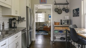 A modern kitchen with white cabinets, a stainless steel refrigerator, and a microwave. There is a dining area with a table and chairs, and a kitchen island with a sink and stools.