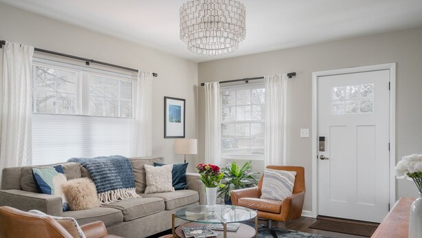 A living room with a sofa, armchairs, a glass coffee table, and a door.