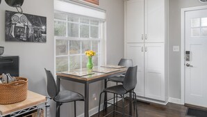 A dining area with a table, chairs, a vase of flowers, and a window with blinds.