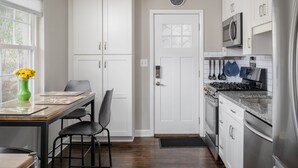 A modern kitchen with white cabinetry, a built-in oven, microwave, and stainless steel appliances. There is a dining table with chairs and a vase of yellow flowers.