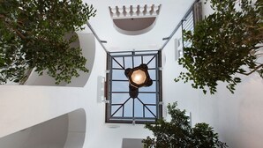 Un cortile con una lanterna al centro, pareti bianche e alberi circostanti.