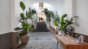 Un corridoio con pavimento in pietra, un tavolo di legno, piante in vaso e una scala che conduce a una stanza con un lampadario.