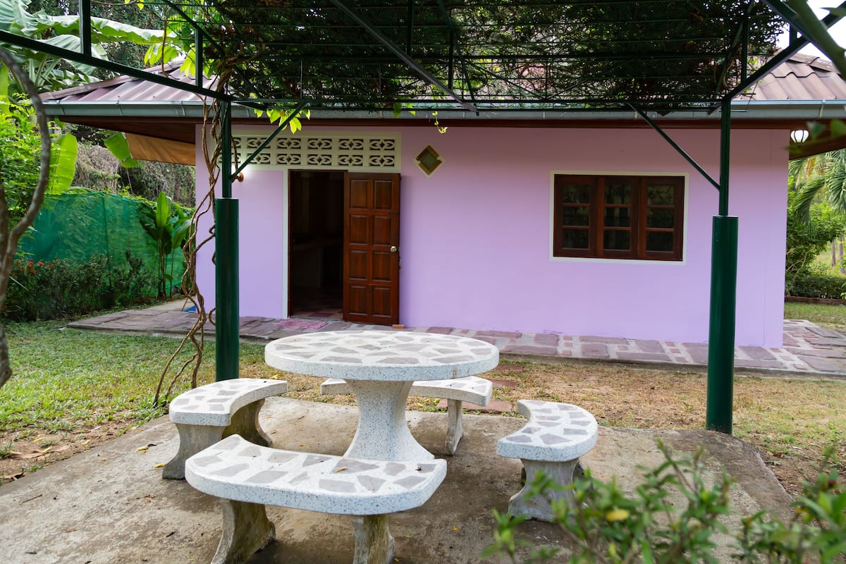 A small building with a purple exterior, a door, and a window. There is a table and four benches in front.