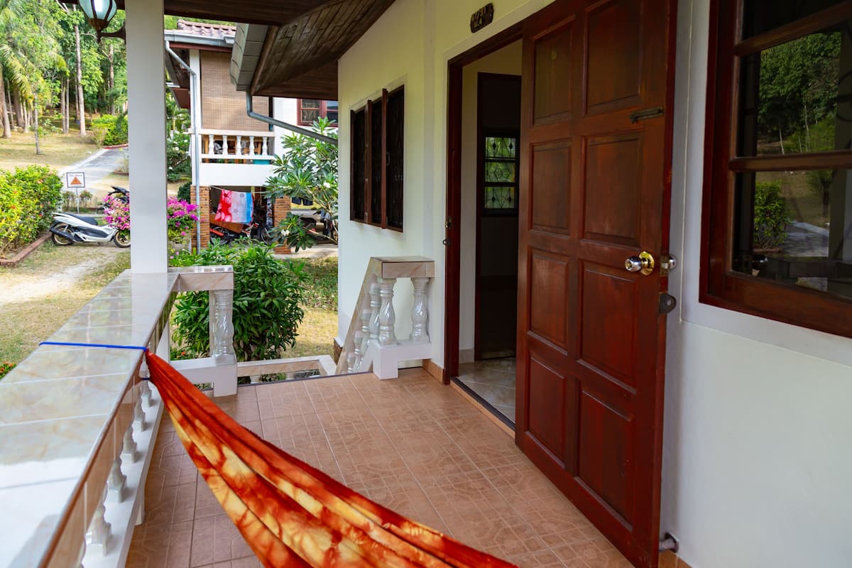 A hotel entrance with a wooden door, a tiled porch, and a view of the surrounding greenery.